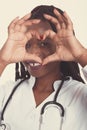 Female american african doctor, nurse woman wearing medical coat with stethoscope doing heart with hands and looking through it. Royalty Free Stock Photo