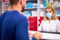 Female apothecary in protective medical mask and young man customer buying drug at drugstore Royalty Free Stock Photo