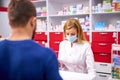Female apothecary in protective medical mask and young man customer buying drug at drugstore Royalty Free Stock Photo