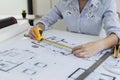 Female architect is using a tape measure to measure the house plans, She is checking the house plans that she has designed before Royalty Free Stock Photo