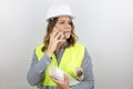 Female architect wearing hardhat,  on white background standing holding plans under arm speaking on phone. Royalty Free Stock Photo