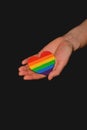 Female arm holding the heart coloured in LGBT pride colours on the dark background. Concept of the International Day Against