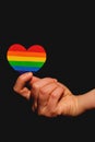 Female arm holding the heart coloured in LGBT pride colours on the dark background. Concept of the International Day Against