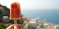 Female arm holding iced strawberry popsicle, blurred sea resort on background, with copy space.