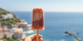 Female arm holding iced strawberry popsicle, blurred sea resort on background, with copy space.