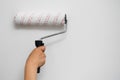 Female arm holding a paint roller against a plain white wall, DIY renovation concept. Royalty Free Stock Photo