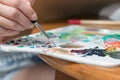 Female artist hand mixing colors with a paintbrush on a color palette