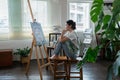 Female artist thinking and hold paintbrush while looking at canvas and pondering about paintin Royalty Free Stock Photo