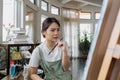 Female artist thinking and hold paintbrush while looking at canvas and pondering about paintin Royalty Free Stock Photo