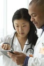 Female Asian doctor talking with African American doctor with tablet Royalty Free Stock Photo