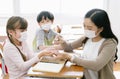 Female Asian teacher with protective face mask and sanitizing school children`s hands with disinfectant spray in classroom after Royalty Free Stock Photo