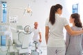 Female assistant talking to girl patient in front of dentist at clinic