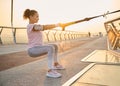 Female athlete practicing body weight training outdoors at sunrise . African sportswoman squatting, exercising with suspension