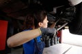 Female auto mechanic inspects the underbody of a car