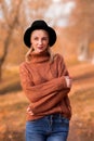 Female autumn portrait. vertical photo of a beautiful blonde girl in a brown warm sweater and black hat stands alone and looks Royalty Free Stock Photo