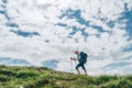 Female backpacker climbing to the mountain top using trekking poles with bright cloudscape background. Active vacation spending by Royalty Free Stock Photo