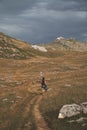 Female backpacker on a grassy field between mountains on a cloudy day at Somiedo Natural Park, Spain