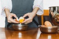 Female baker with apron cracking an egg prepare for baking on wooden table