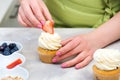 Female baker decorating cupcake with strawberry at table. Process of decorating cupcakes