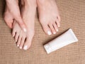 Female bare feet with white pedicure and tube of cream on canvas fabric, close up.