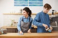 Female barista sponging down table smiling happily. Make pouring coffee.