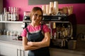 female barista stands with her arms crossed on her chest and professional coffee machine in the background