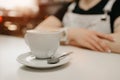 Female barista waits with a cup of coffee with a saucer and spoon for a client