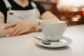 Female barista waits with a cup of coffee with a saucer and spoon for a client