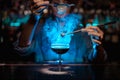 Female bartender adding to a brown cocktail and pour on a flamed badian on tweezers a powdered sugar in the blue light Royalty Free Stock Photo