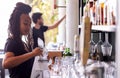 Female Bartender Cleaning Glasses With Cloth Behind Bar