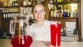 Female bartender in eyeglasses with juice in glass and jug on bar counter, standing behind bar, looking at camera Royalty Free Stock Photo