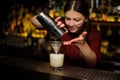 Female bartender pouring out a cocktail from the shaker through the bolter