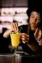 Female bartender puts a sprig of rosemary on the finished Blood orange paloma cocktail at the bar