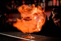 Female bartender serving on fire alcoholic transparent cocktail with ice in the glass decorated with a pink rose bud