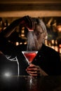 Female bartender sprinkling the orange peel into the cocktail glass filled with brown alcoholic drink