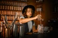 Female bartender stirs ice in a glass with a long bar spoon to prepare a cocktail