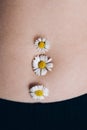 Female beautiful tummy with a chamomile flower in the navel. Perfect body shape