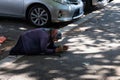 Female beggar with headscarf begs for money kneeling on a sidewalk