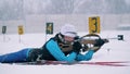 Female biathlete is lying in the shooting zone with a rifle