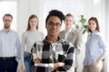 Female black millennial employee standing foreground arms crosse Royalty Free Stock Photo