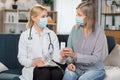 Female blond professional doctor consulting senior patient during medical care visit at home. Woman physician explaining Royalty Free Stock Photo