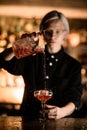 Female blonde bartender enjoying the process of pouring a cocktail into a glass with ice so that the drink splashes to Royalty Free Stock Photo