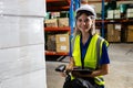 Female blonde hair factory company employee scanning box checking number of products on goods shelves with tablet in warehouse.