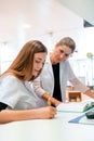 Female blonde pharmacist helps and assists her young aprrentice trainee during studies of medical books Royalty Free Stock Photo