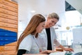 Female blonde pharmacist helps and assists her young aprrentice trainee during studies of medical books Royalty Free Stock Photo