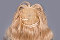 Female blonde wig close up on grey background. Golden human hair weaves, extensions and wigs. Woman beauty concept