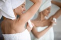 After shower woman wrapped in towel apply at armpit antiperspirant