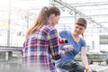 Female botanist pouring coffee for coworker in greenhouse