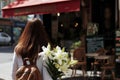 female with a bouquet of lilies, walking past a streetside caf