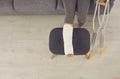 Female broken injured leg relaxing on stool in cast and metal crutches